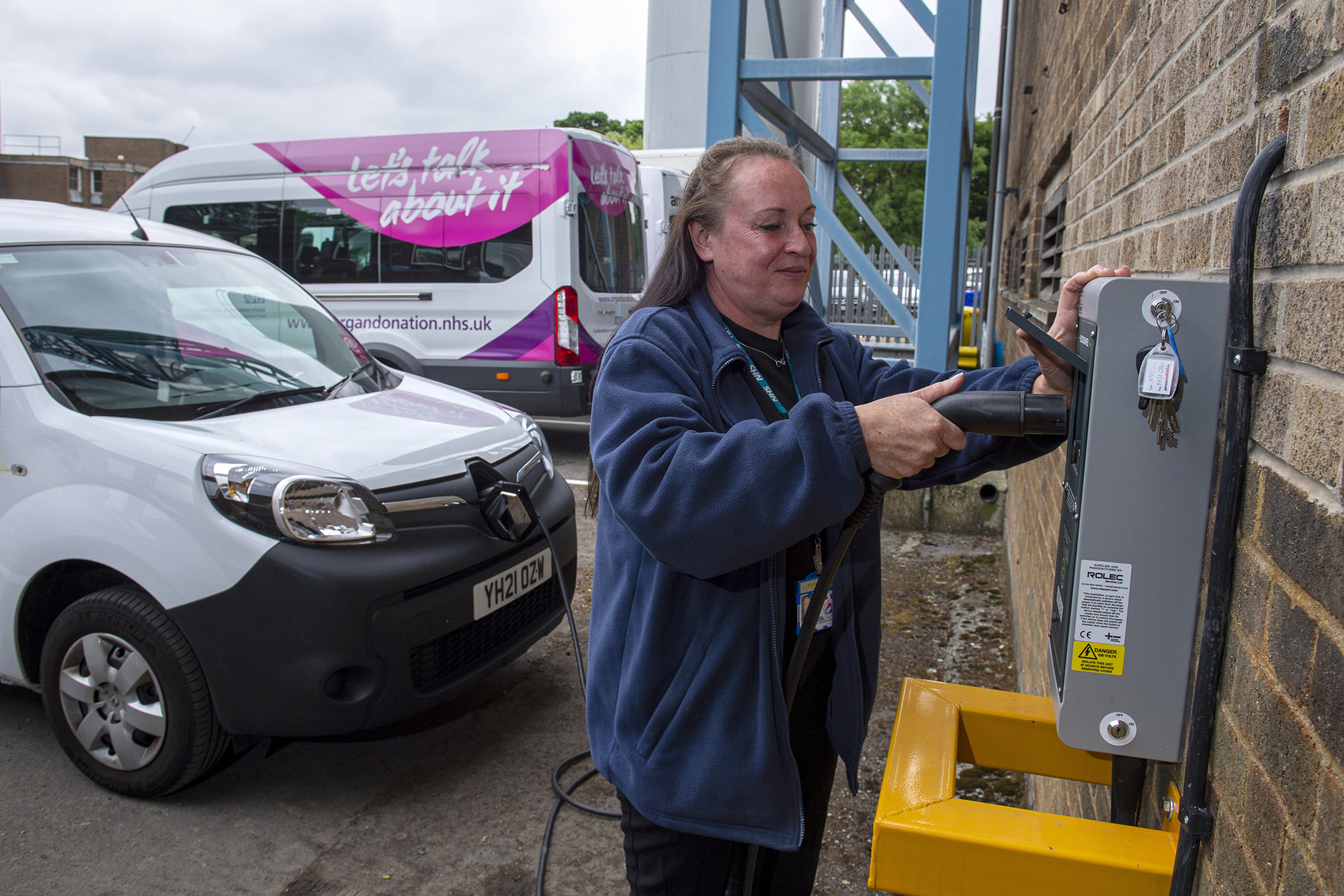 Female employee plugging in an EV charger into the wall unit