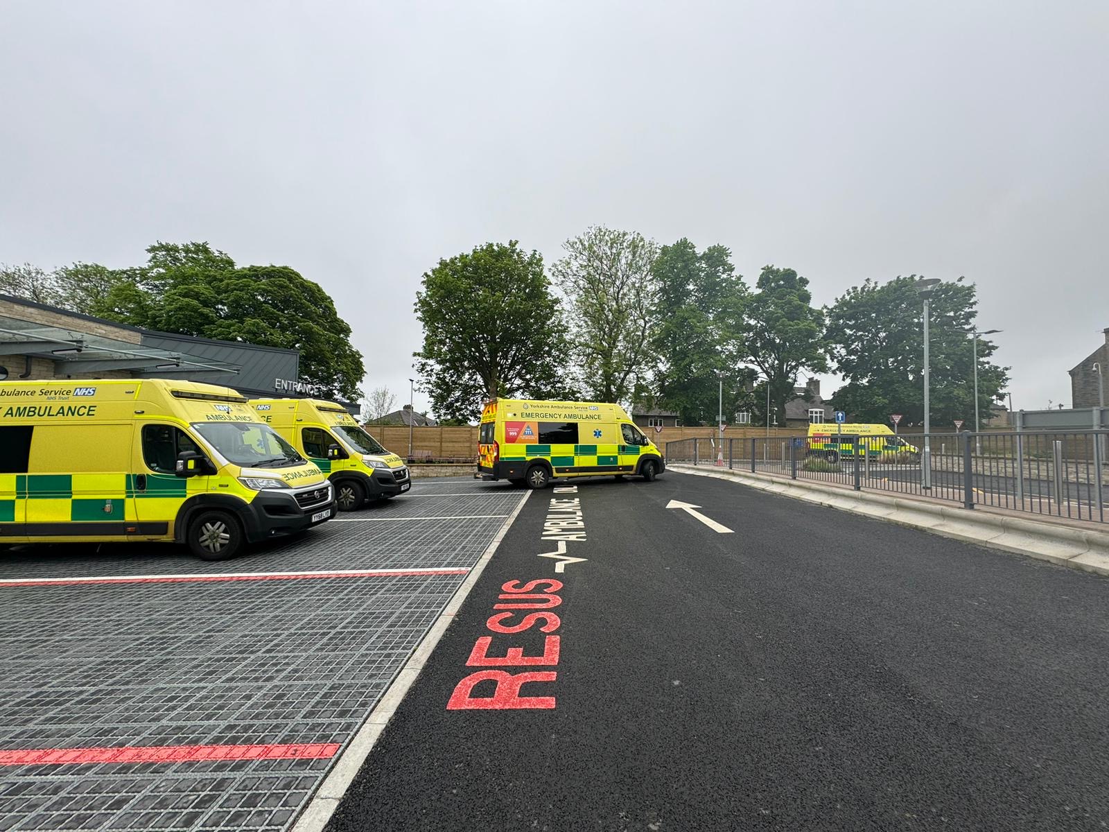 Ambulance bays at Huddersfield A&E with 2 ambulances parked, 1 leaving and 1 entering in the distance.