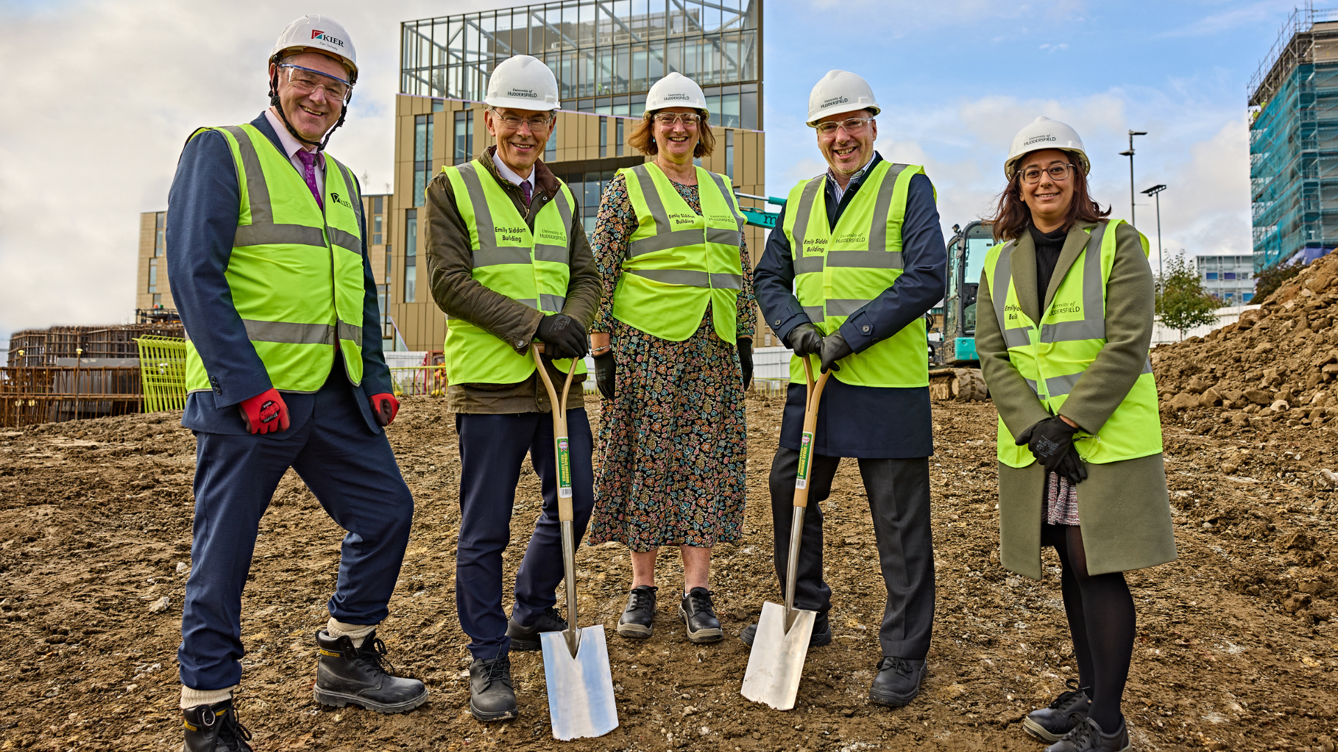 A group of people in high vis vests and hard hats holding spades on a construction site