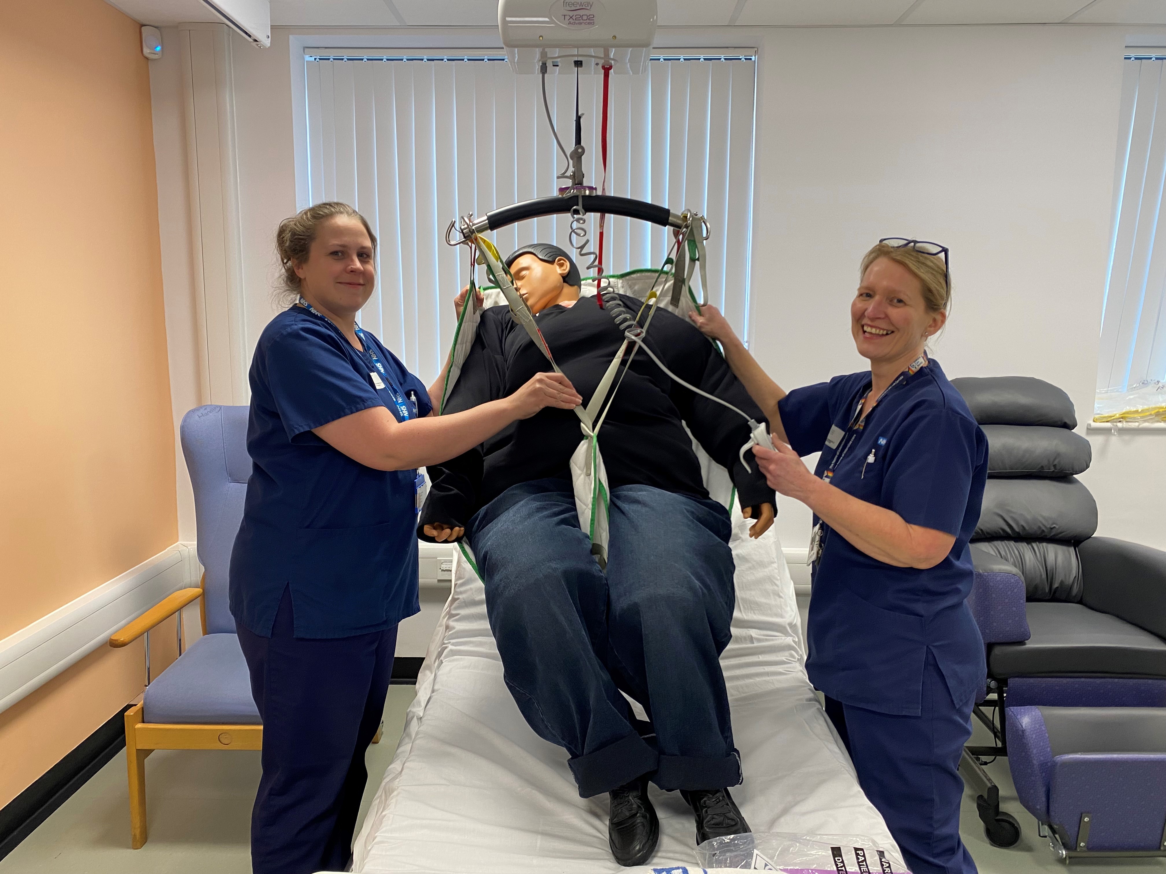 Two colleagues stood by a mannikin in a hoist used for bariatric patients 
