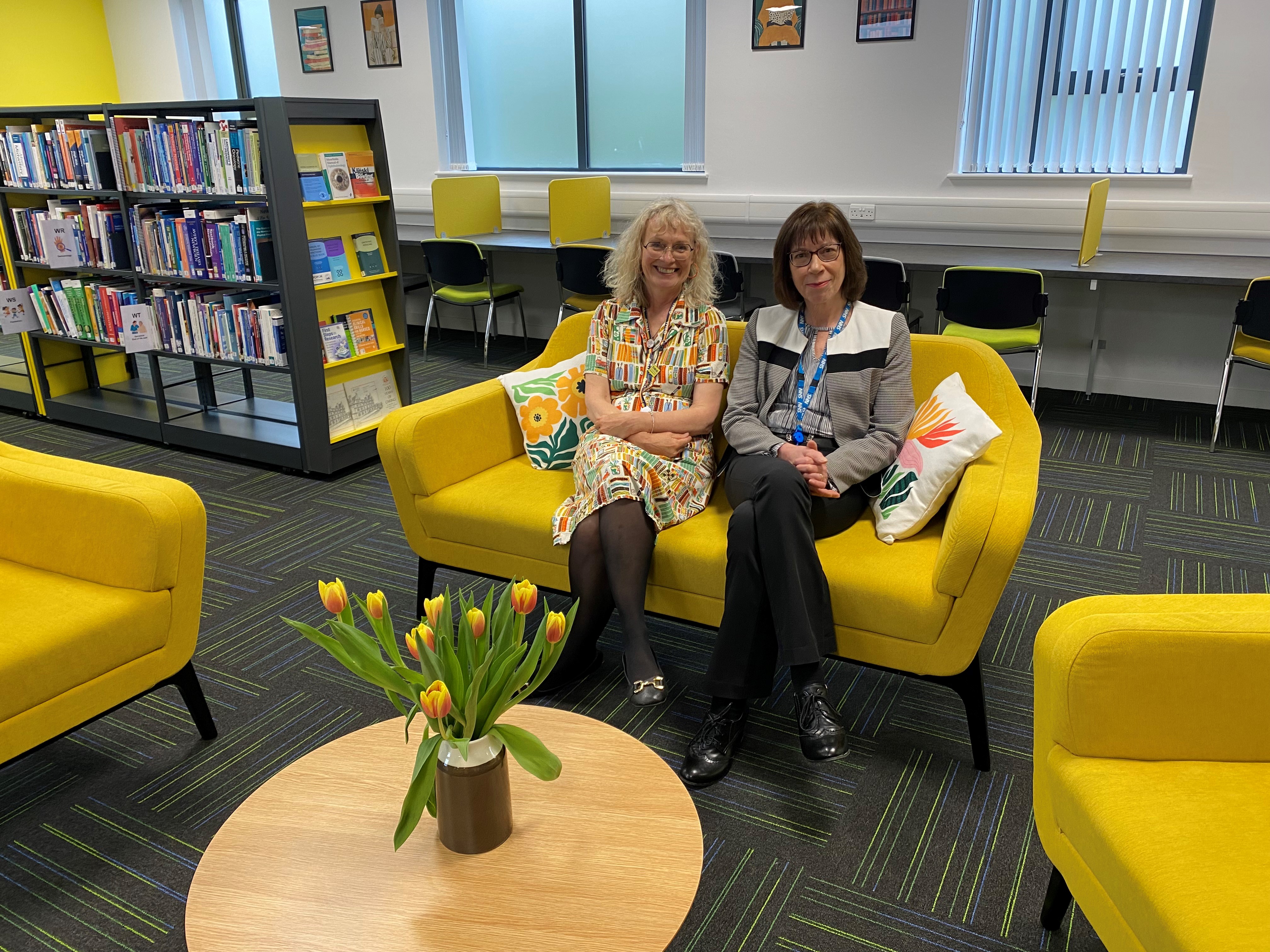 Colleagues sat on a bright yellow chair in our new library area