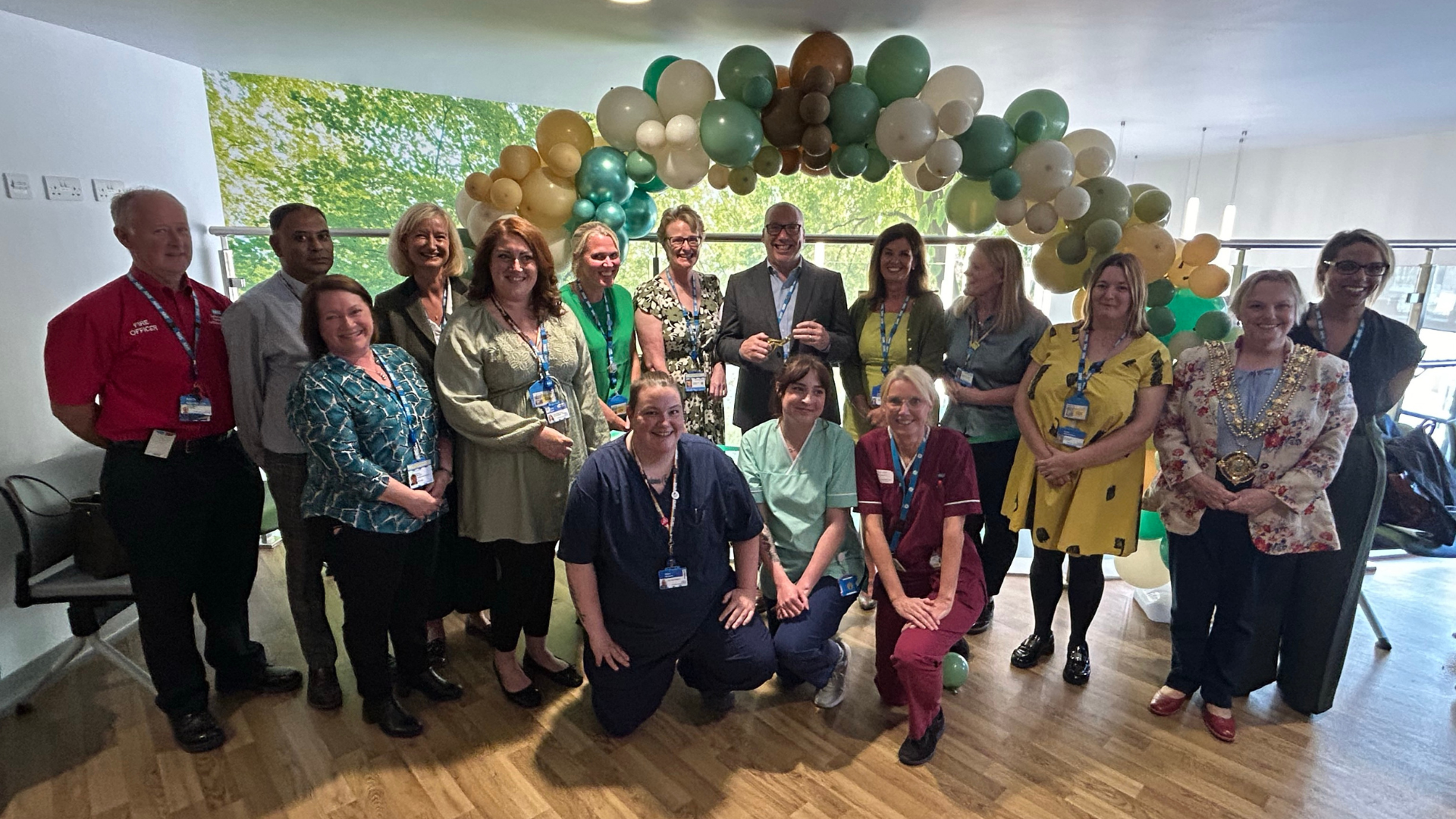 A group of people standing under a balloon arch. Brendan Brown holds a pair of scissors in the middle of the group preparing to cut the ribbon