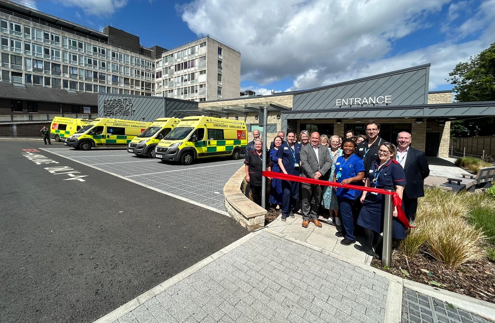 Dr Mark Davies and colleagues stand in front of the new A&E cutting a red ribbon. There are ambulances in the background