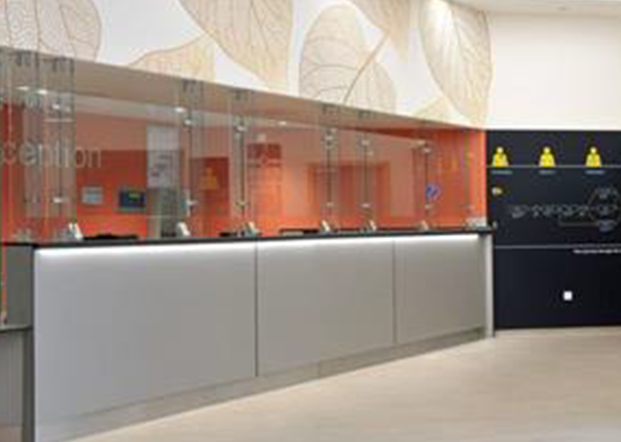 Reception desk with an orange wall and a glass barrier above the desk.