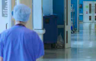 A clinical member of staff is walking down a very clean corridor in a hospital environment.
